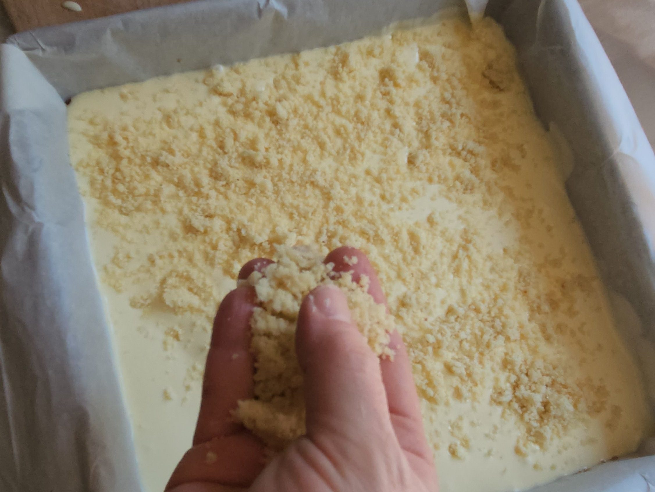 sprinkling the crumble mixture on the top of the easy almond cheescake bars