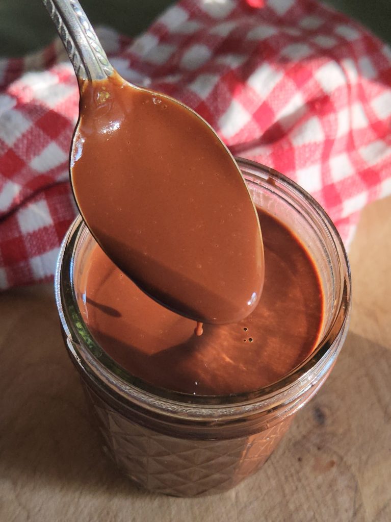 homemade low carb gluten free chocolate syrup in a jar dipped from a spoon