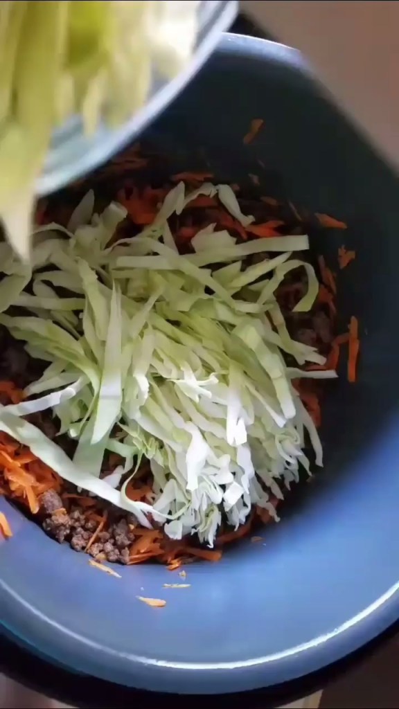 Fresh cabbage and carrots being added to the instapot low carb egg rolls and a bowl