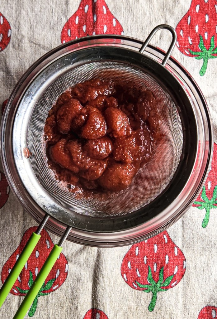 pouring stewed strawberries into strainer over bowl.