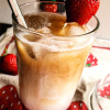Easy Dairy Free Iced Strawberry Latte in a glass adorned with a strawberry on the rim with a straw.
