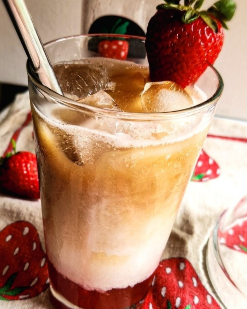 Easy Dairy Free Iced Strawberry Latte in a glass adorned with a strawberry on the rim with a straw.