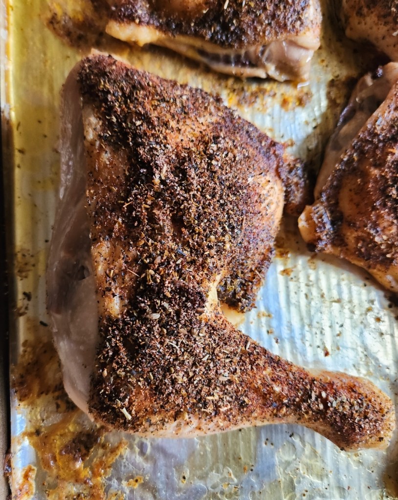 baked chicken leg quarters covered in spices on a baking sheet.