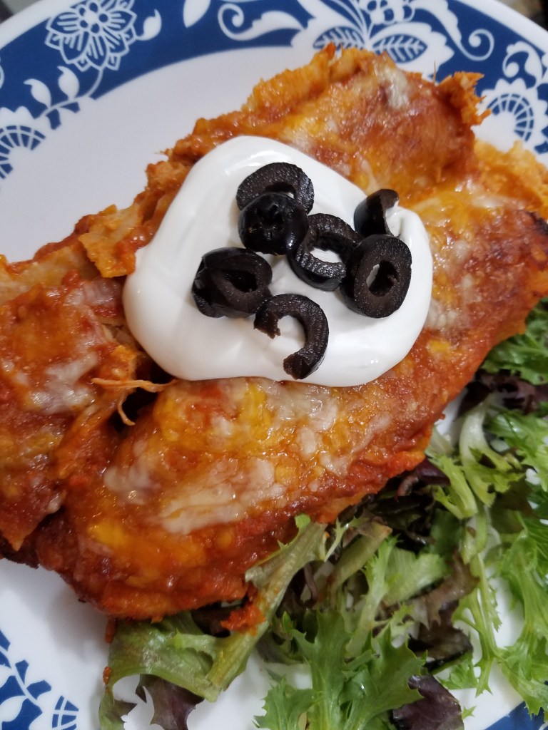 chicken enchiladas rolled on a plate with lettuce sour cream and black olives.
