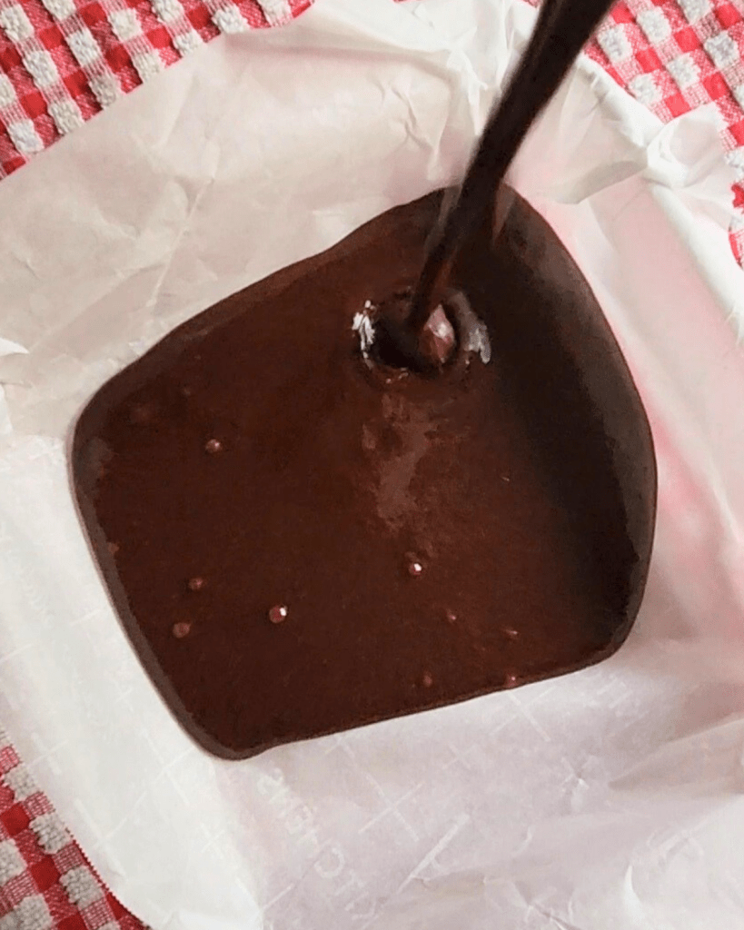 Homemade Brownie Batter being poured into a parchment lined pan before freezing