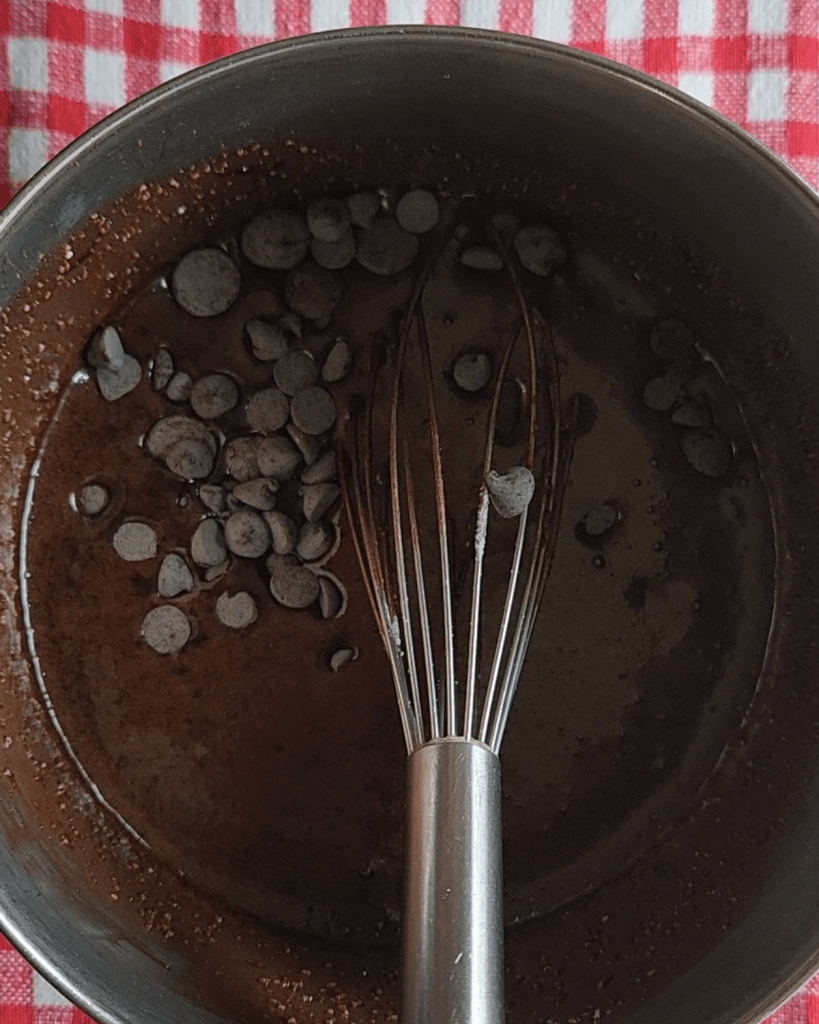 brownie batter in a pan with a whisk and chocolate chips