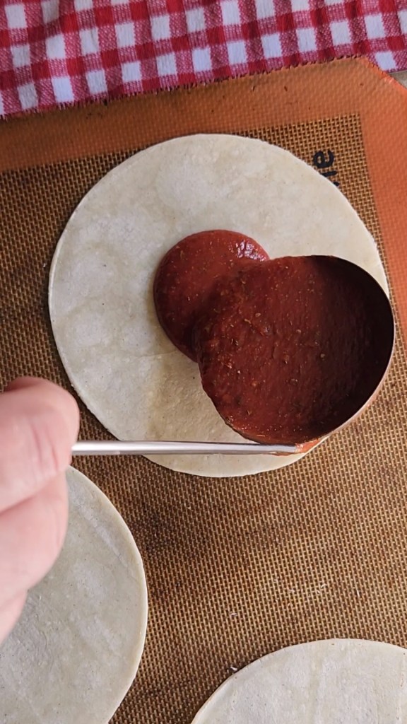 low carb tortillas laid on a silpat lined pan with sauce poured in the middle.