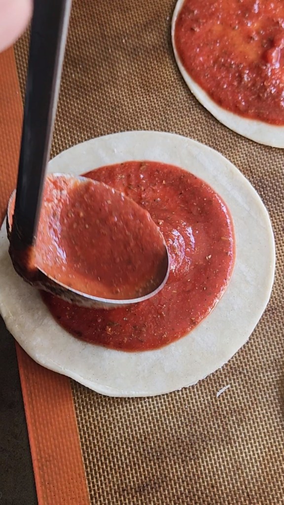 spreading the pizza sauce in a circle on the surface of the tortilla.