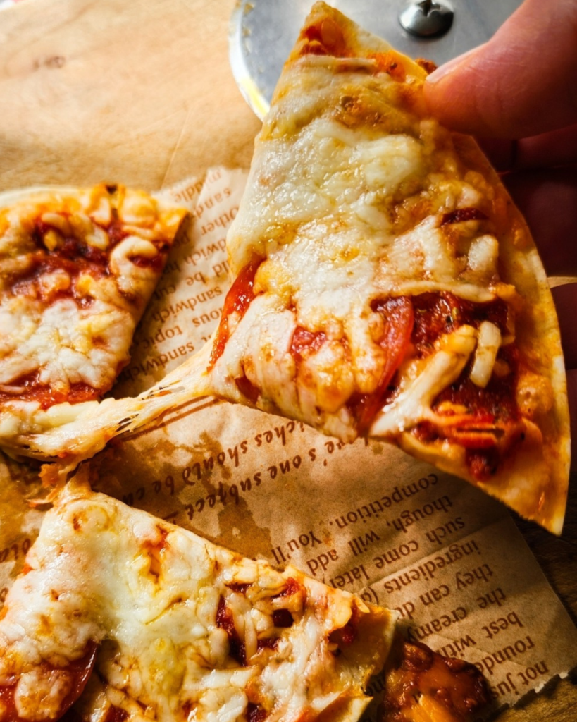 a piece of easy gluten free low carb tortilla pizza recipe being pulled apart.