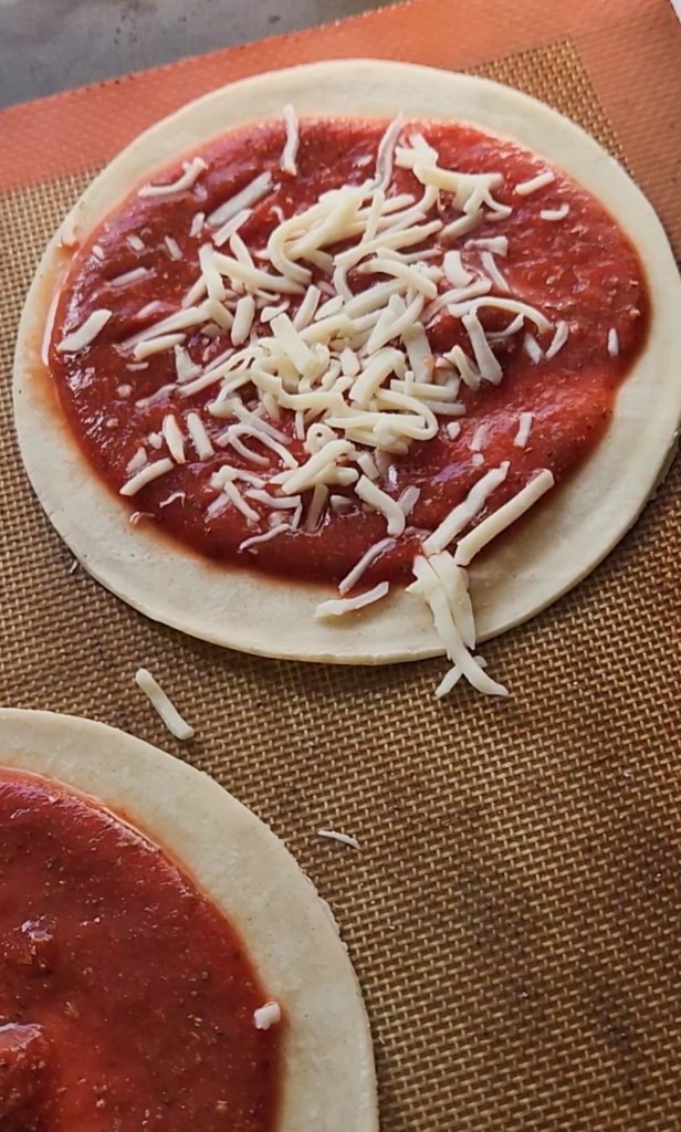 sprinkling mozzarella on top of the pizza sauce spread on the low carb tortilla.