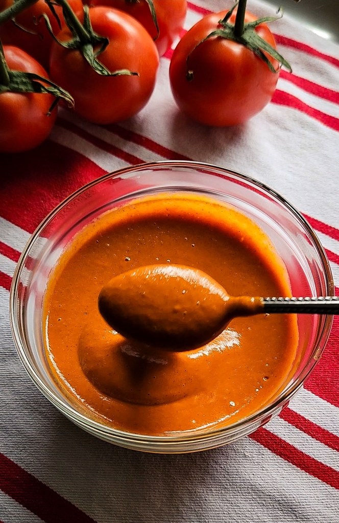 Dipping up easy low carb enchilada sauce from a bowl with a spoon.