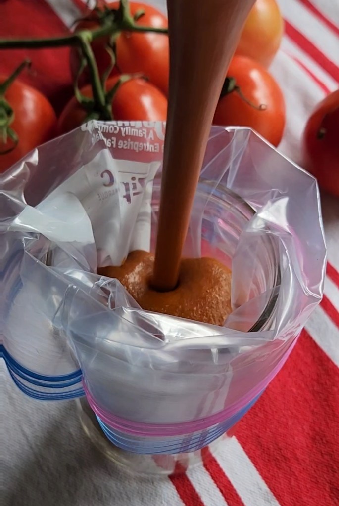 Easy low carb enchilada sauce being poured into a gallon Ziploc bag that has been fitted into a wide mouth jar.
