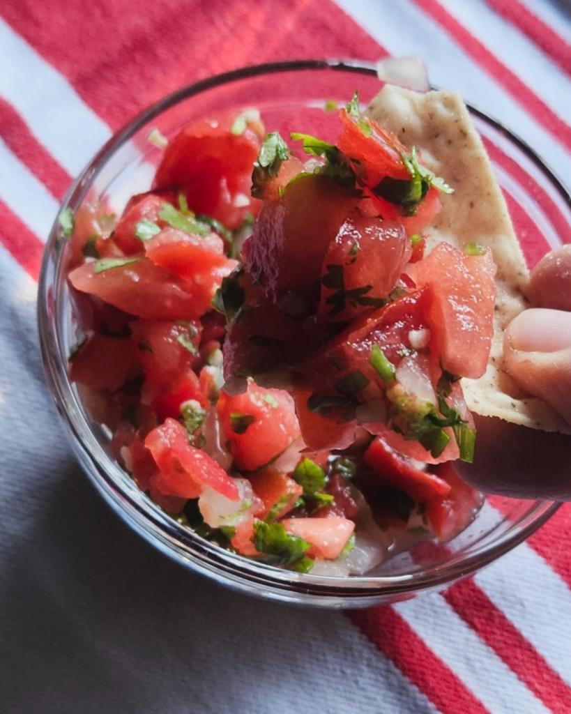 fresh pico de gallo being dipped into with a tortilla chip.