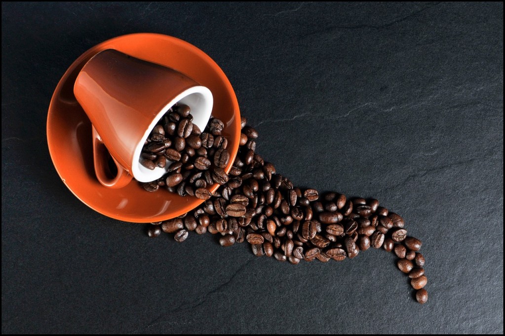 Whole coffee beans spilling out of a coffee cup.