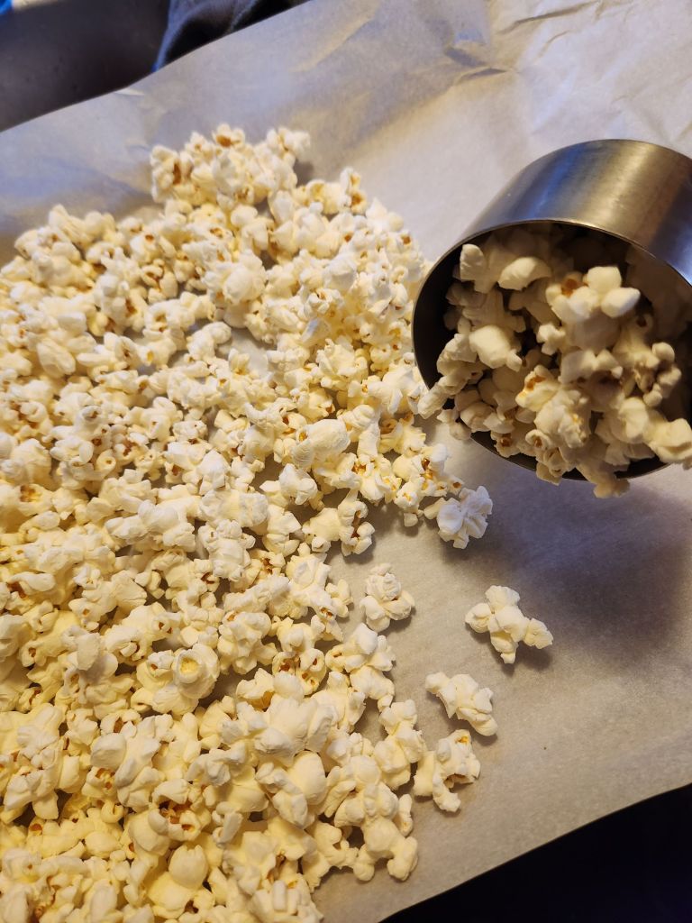 Spreading playing popcorn on a parchment lined baking sheet.