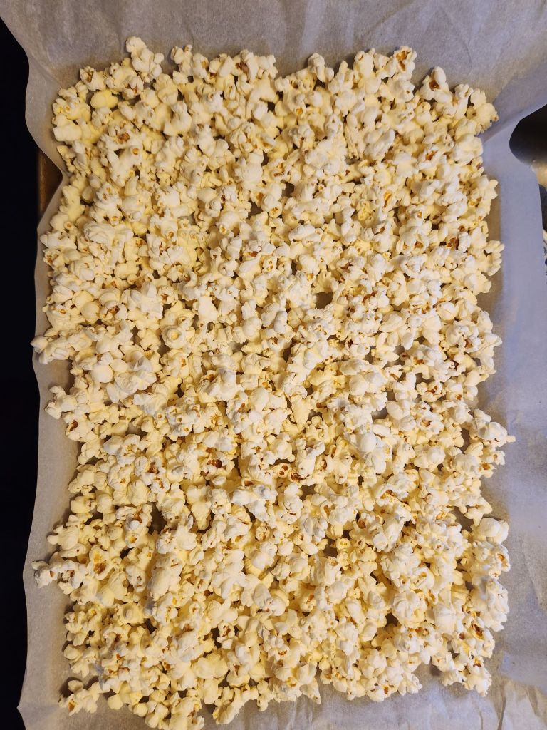 Plain popcorn spread out on a parchment lined baking sheet.
