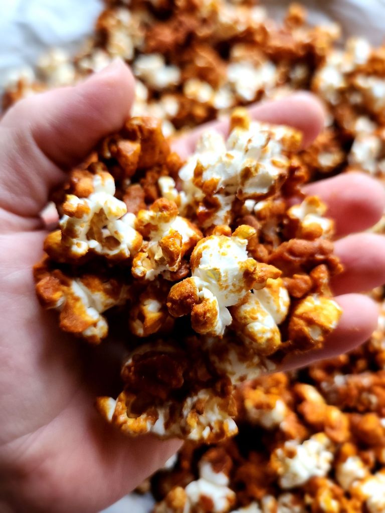 A hand holding low-carb caramel popcorn made without corn syrup.