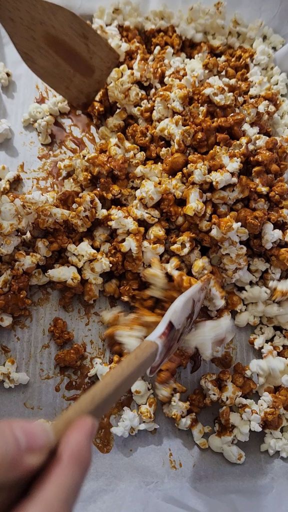 Stirring up low carb caramel popcorn without syrup on a baking sheet.
