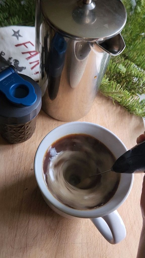 Mixing low-carb gingerbread syrup and coffee in a mug with a stick wand.