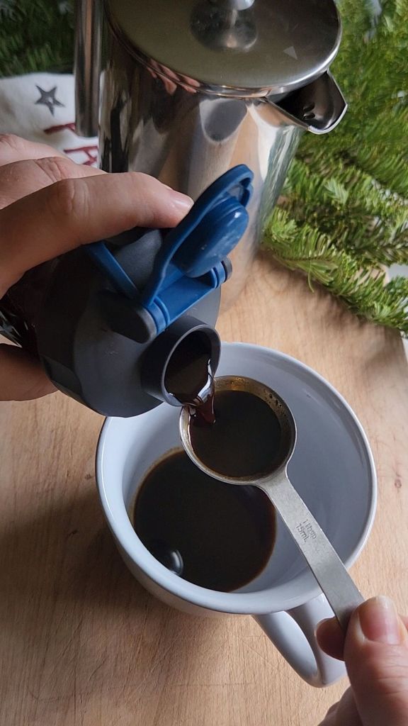 Pouring low carb copycat Starbucks gingerbread syrup into a coffee mug to make a latte.
