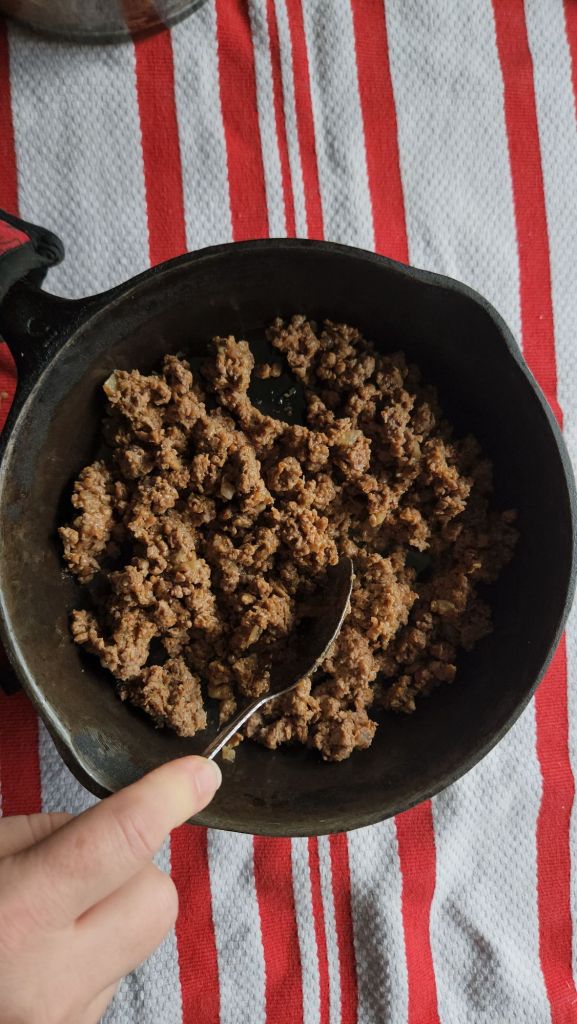 leftover taco meat being reheated in a cast iron skillet being stirred with a spoon.