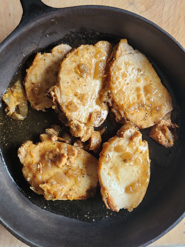 Cooked pork loin sliced in a cast iron skillet for warming.