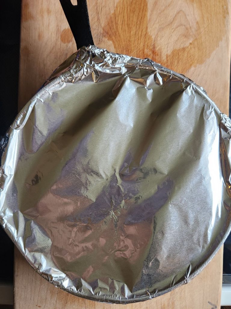 Oven proof Skillet with foil containing cooked pork loin for warming.