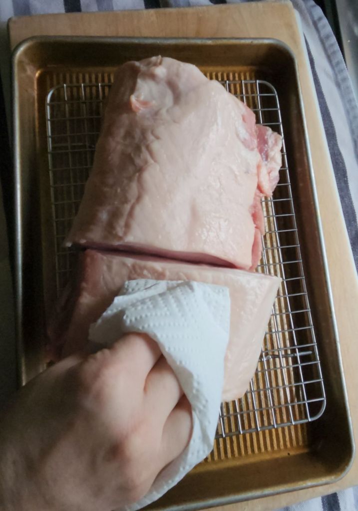 Patting a raw pork loin dry with paper towels.