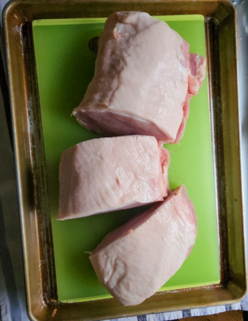 Raw pork loin cut into thirds on a cutting board.