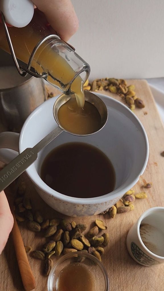 Pouring the low carb copycat Starbucks pistachio latte syrup into the white mug with coffee.
