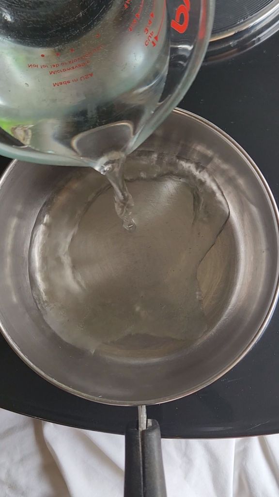 Pouring water into a small saucepan to make low carb copycat Starbucks pistachio latte syrup.