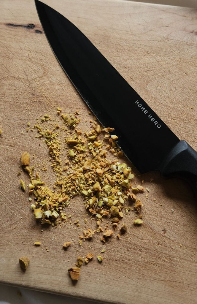 Hand chopped pistachios on a cutting board with a chef's knife.