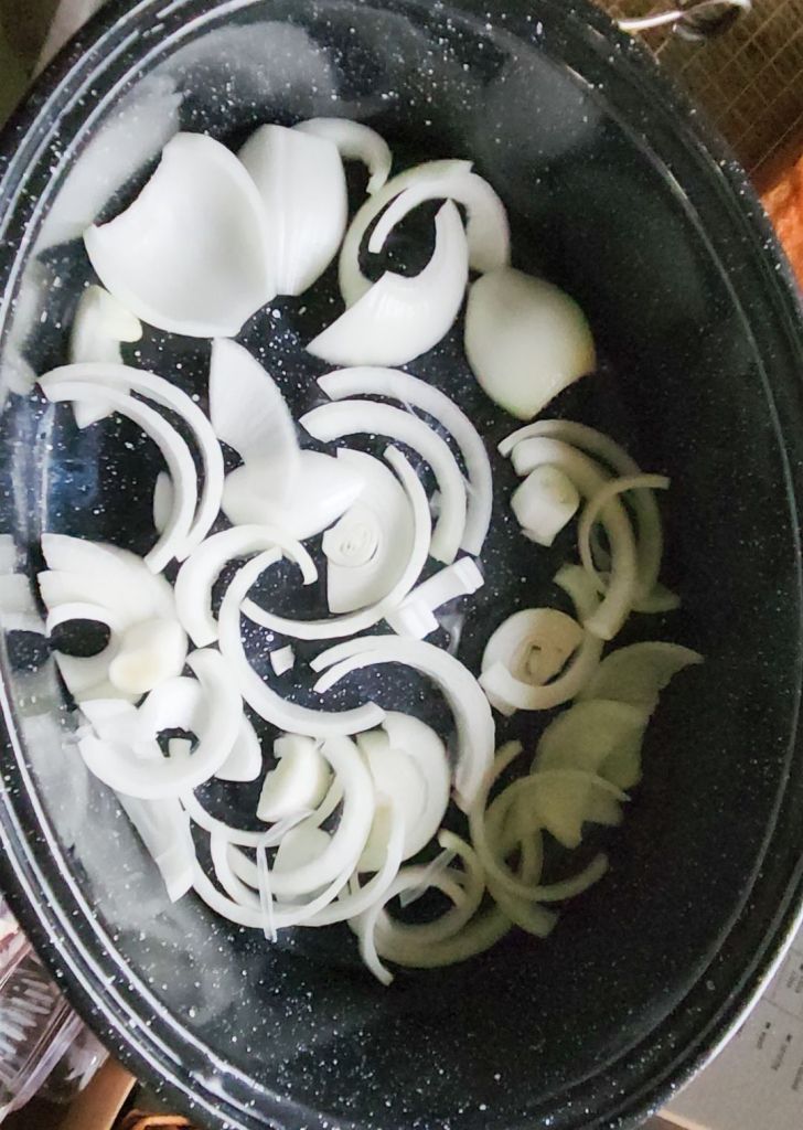 Raw onion rings layered and bottom of black roasting pan.