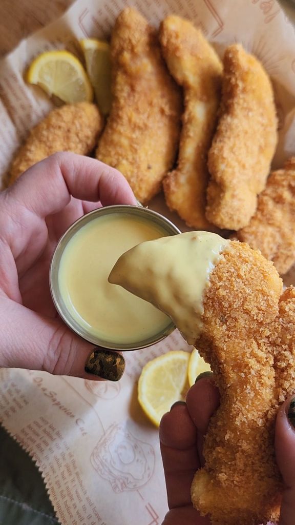 Dipping air fryer Keto Chicken Strip in low carb honey mustard.