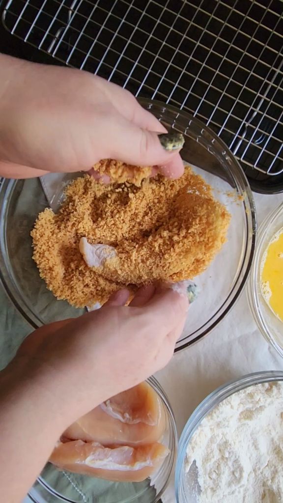 Dipping chicken tender in crushed pork rinds.