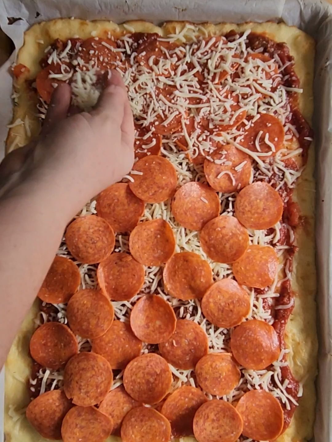 Finishing topping the best gluten-free keto friendly pizza with cheese.