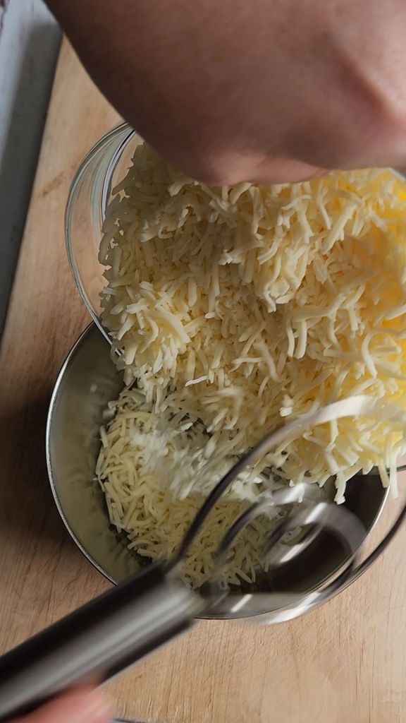 Pouring cheeses into a saucepan for melting.