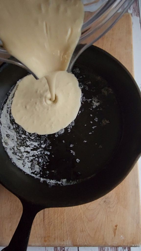 The best gluten-free keto Dutch baby pancake recipe batter being poured into a hot cast iron skillet.