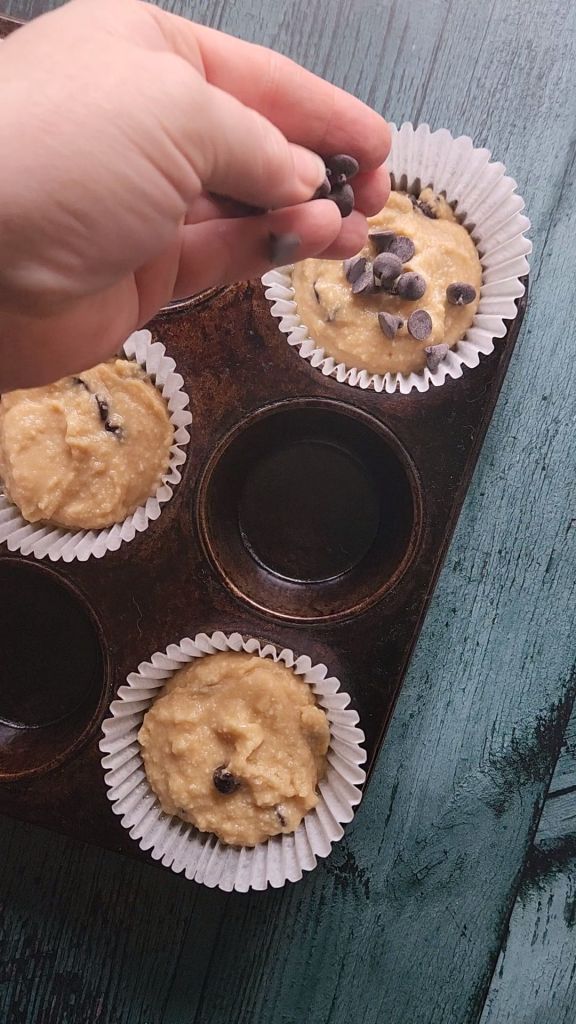 Scooping Bakery style gluten-free chocolate chip muffin batter into the muffin tin.