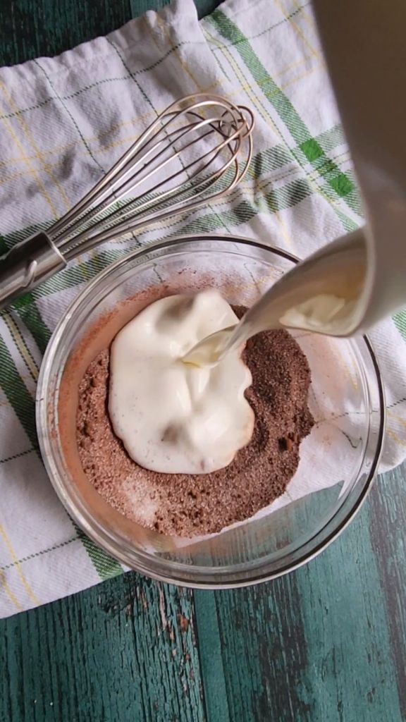 Heavy cream being added to the bowl of dry ingredients for the best low carb copycat keto Baileys Irish Cream recipe.
