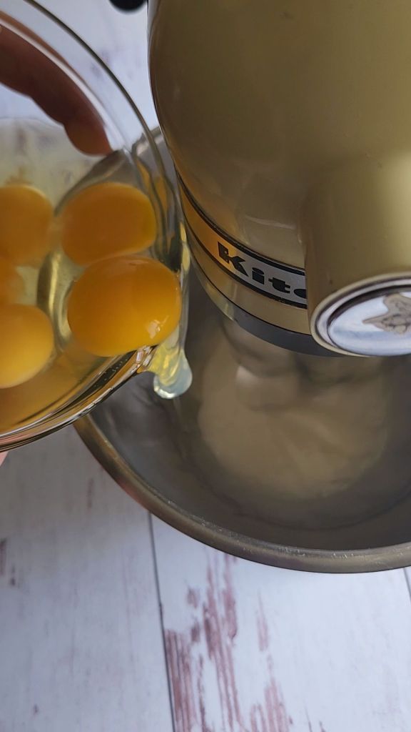 Adding eggs one at a time making the best gluten-free strawberry pudding cake recipe.