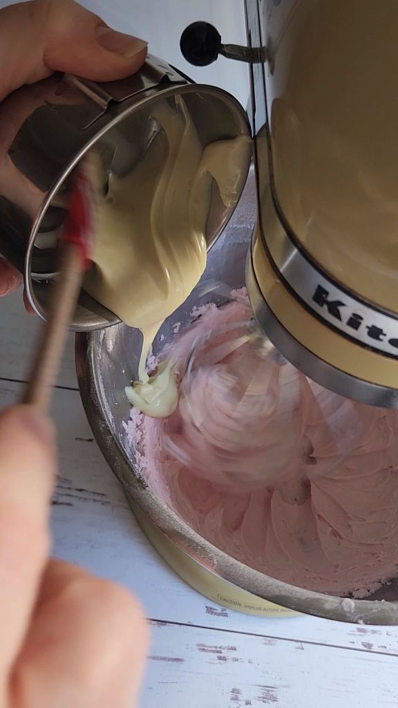 Pouring melted sugar-free white chocolate chips into the sugar-free strawberry frosting.