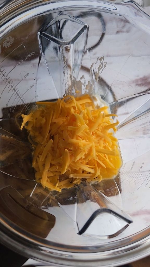Adding shredded cheddar cheese to the blender to make gluten-free keto copycat Starbucks egg bites recipe.