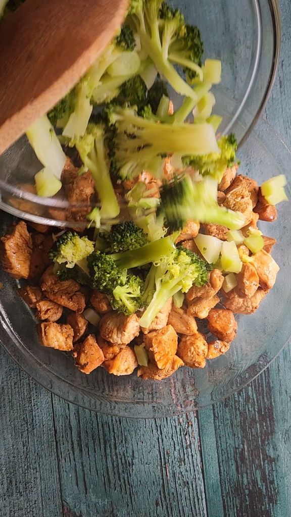 Pouring broccoli on top of chicken in pie plate.