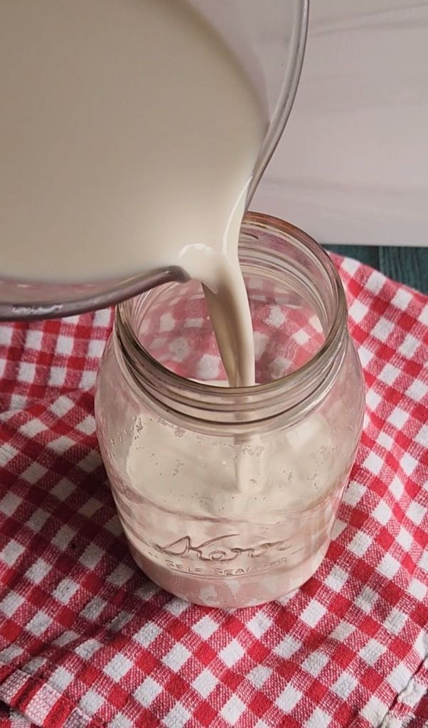 Pouring strained almond milk into a glass quart jar.
