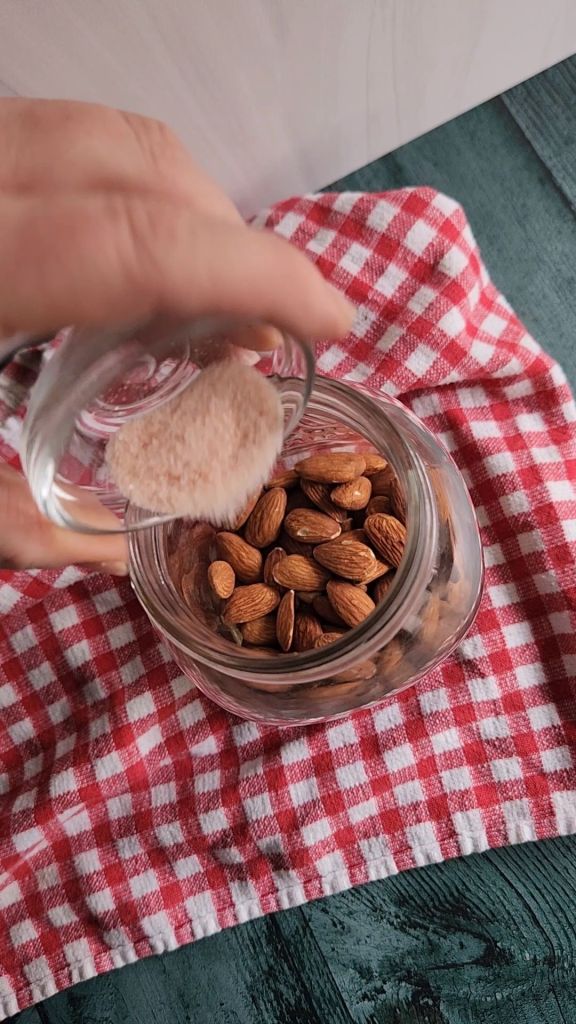 Adding sea salt to raw almonds in quart jar.