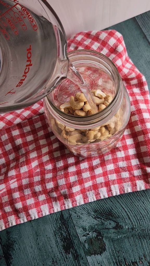 Pouring water into jar of raw cashews to soak overnight.