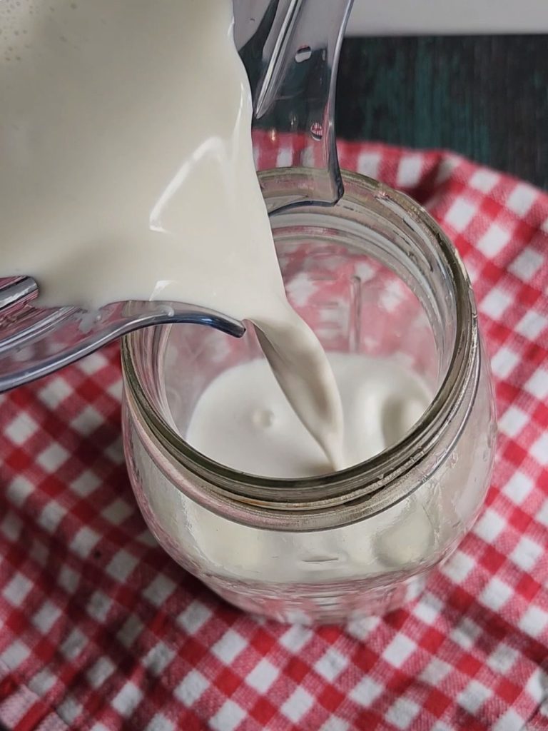 Pouring prepared nut milk into a glass quart jar.