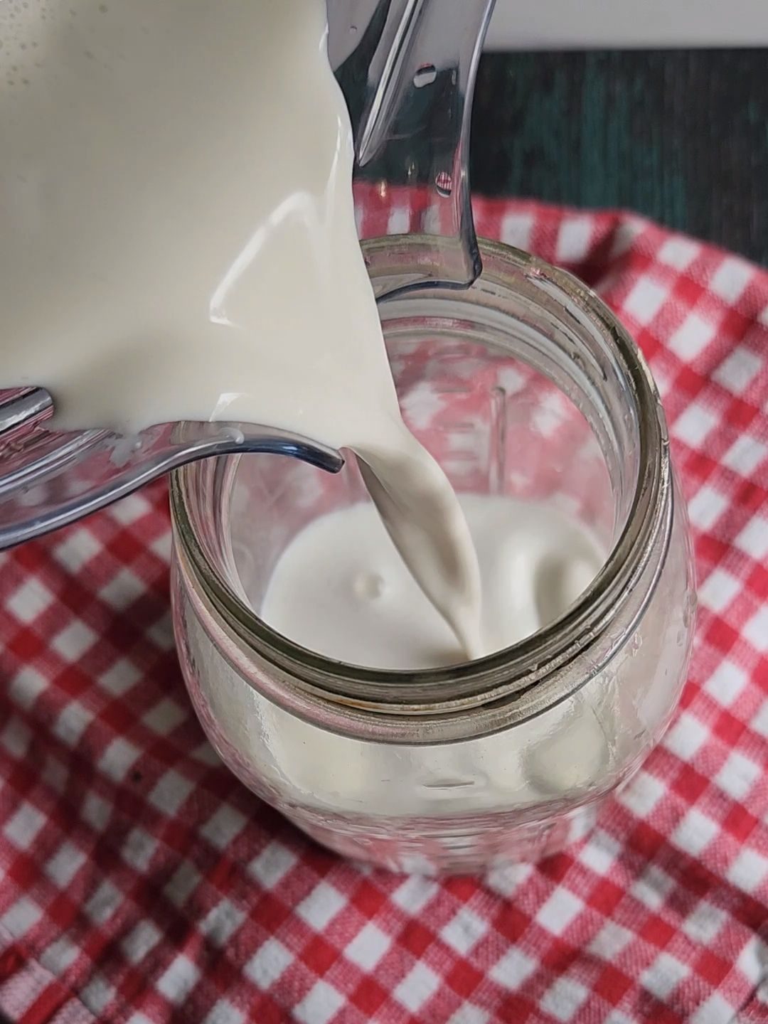 Pouring prepared nut milk into a glass quart jar.