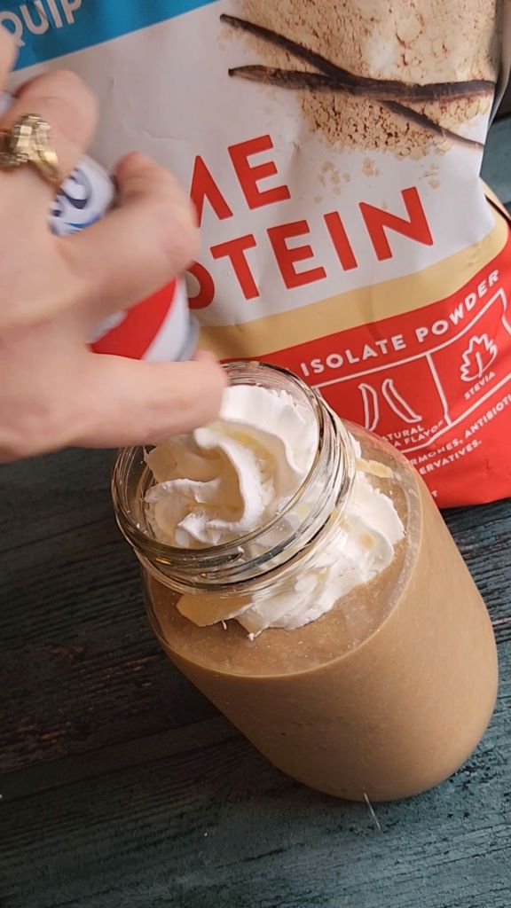Putting whipped cream onto the top of my dairy-free high protein almond mocha smoothie recipe.